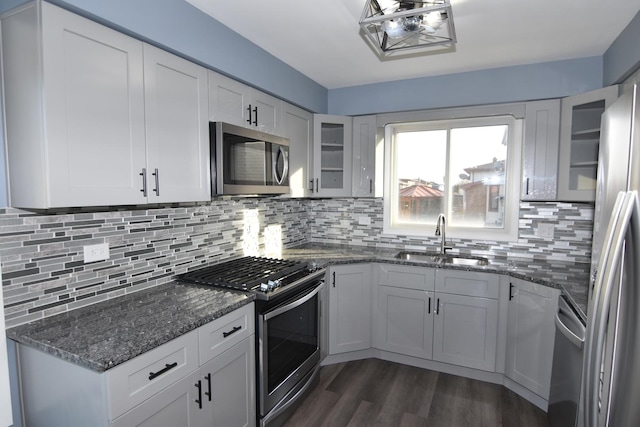 kitchen with a sink, white cabinetry, appliances with stainless steel finishes, decorative backsplash, and glass insert cabinets