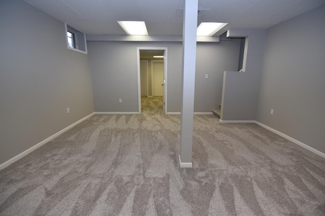 basement featuring light carpet, baseboards, and a paneled ceiling