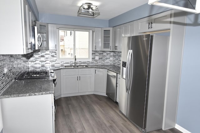 kitchen featuring dark wood finished floors, backsplash, appliances with stainless steel finishes, glass insert cabinets, and a sink