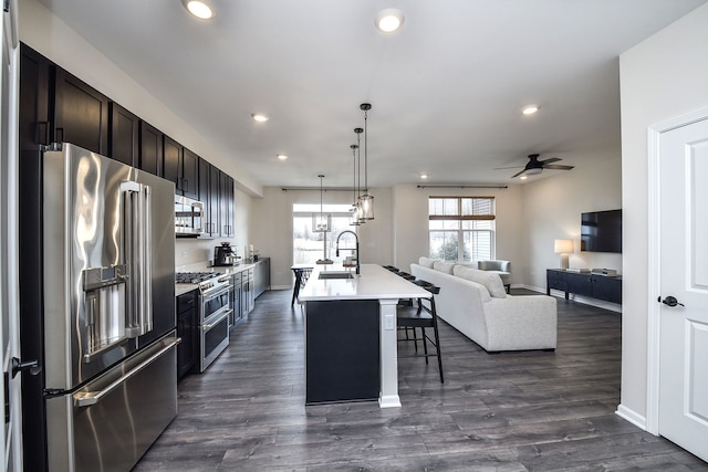 kitchen with sink, a center island with sink, stainless steel appliances, a kitchen bar, and dark hardwood / wood-style flooring