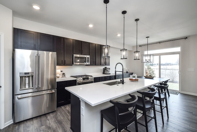 kitchen with sink, a breakfast bar, appliances with stainless steel finishes, a kitchen island with sink, and hanging light fixtures