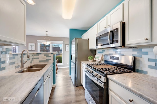 kitchen featuring sink, white cabinetry, light wood-type flooring, pendant lighting, and stainless steel appliances