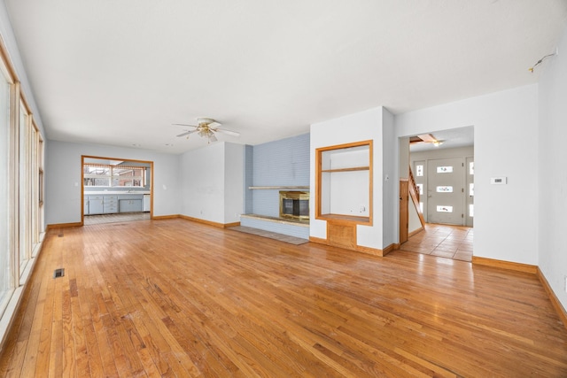 unfurnished living room with a fireplace, ceiling fan, and light wood-type flooring