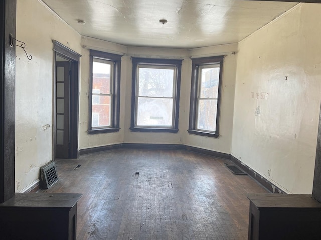 empty room with wood-type flooring, visible vents, and baseboards