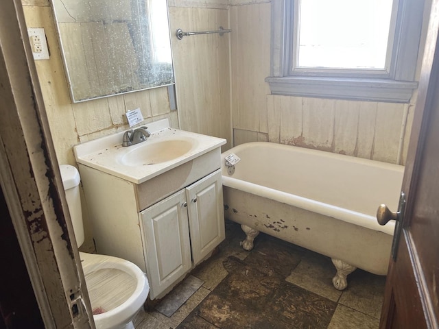 bathroom featuring toilet, a bathing tub, stone finish floor, and vanity