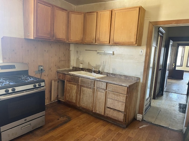 kitchen with gas range, dark wood-style flooring, a sink, and brown cabinetry