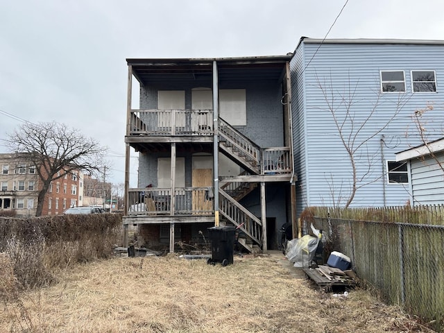 back of property with brick siding, fence, and stairs