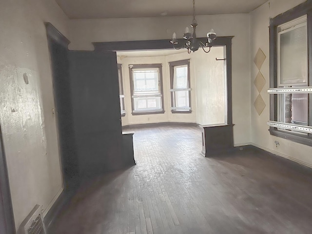 unfurnished dining area featuring dark wood-style flooring, visible vents, a notable chandelier, and baseboards