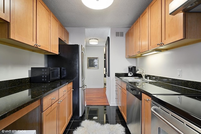 kitchen featuring sink, extractor fan, a textured ceiling, appliances with stainless steel finishes, and dark stone counters