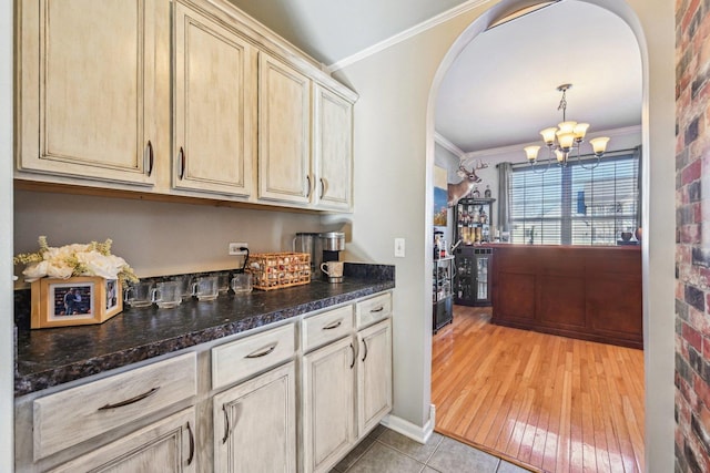 bar featuring dark stone countertops, hanging light fixtures, a notable chandelier, ornamental molding, and cream cabinetry