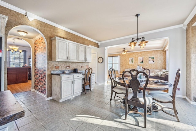 dining room with light tile patterned flooring, ornamental molding, and ceiling fan with notable chandelier