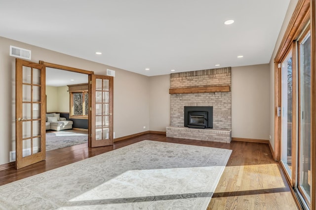 living room with a brick fireplace, a healthy amount of sunlight, hardwood / wood-style floors, and french doors