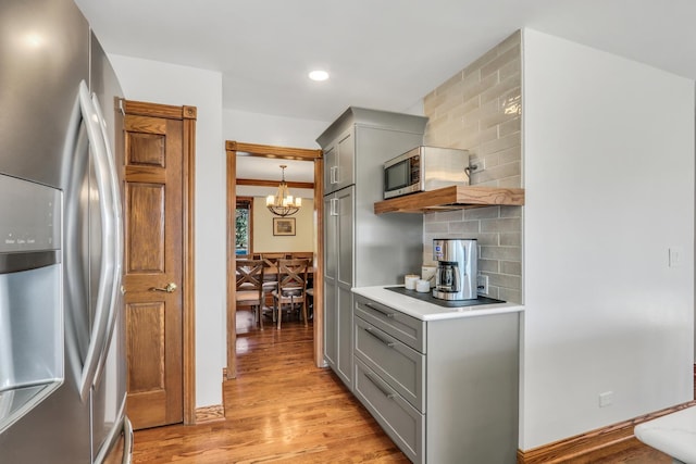 kitchen with light hardwood / wood-style flooring, appliances with stainless steel finishes, gray cabinetry, backsplash, and decorative light fixtures