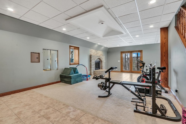 exercise room with light colored carpet, electric panel, a brick fireplace, and a drop ceiling