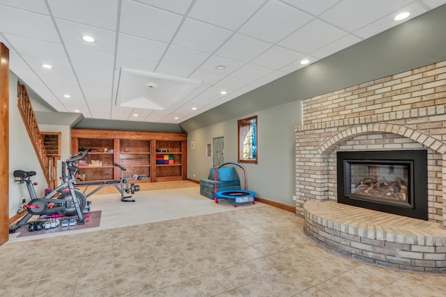 workout area with a paneled ceiling, tile patterned flooring, and a brick fireplace