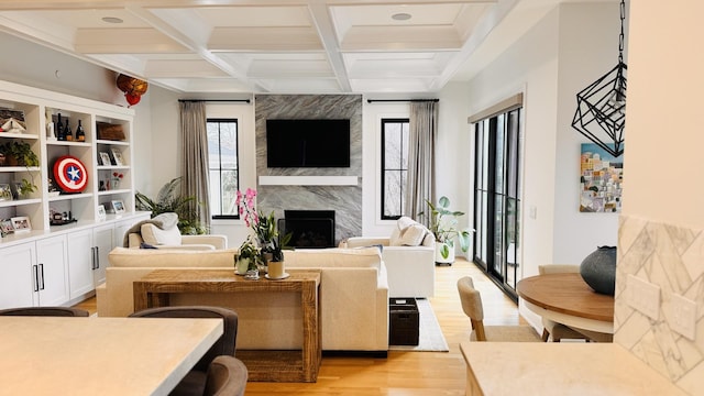 living room featuring beamed ceiling, a fireplace, coffered ceiling, and light wood-style floors