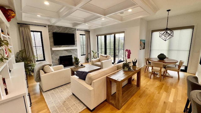 living room featuring plenty of natural light, light wood-style flooring, a fireplace, and coffered ceiling