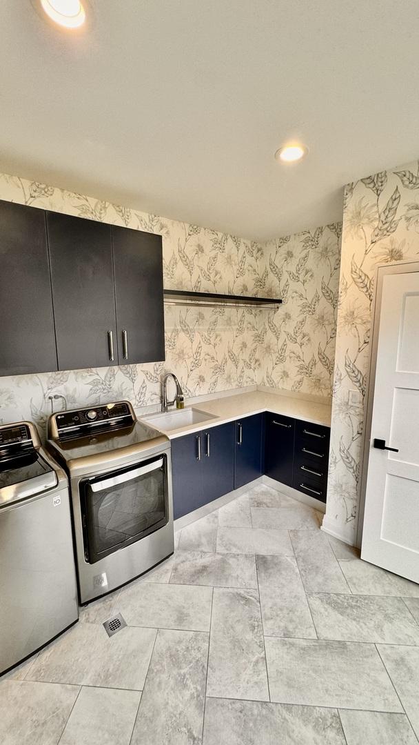 laundry room featuring cabinet space, wallpapered walls, washer and dryer, a sink, and recessed lighting