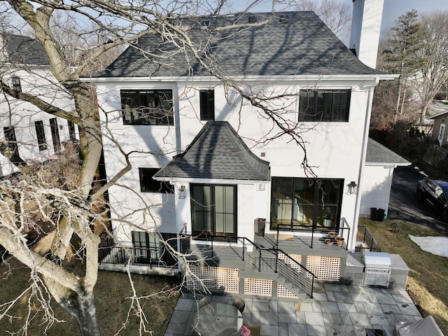 rear view of property featuring a chimney and roof with shingles