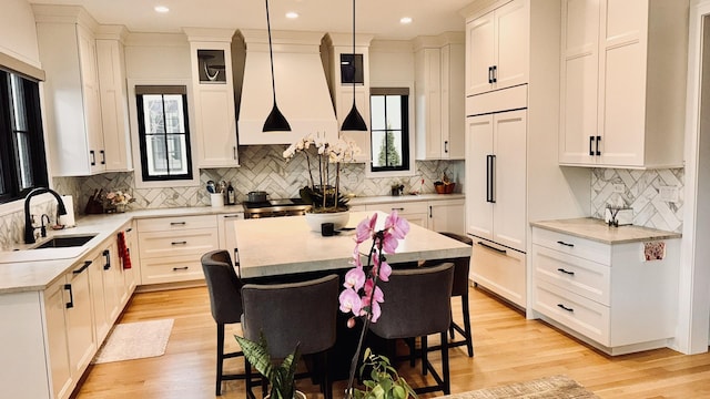 kitchen featuring a kitchen island, a sink, a kitchen breakfast bar, custom exhaust hood, and light wood finished floors