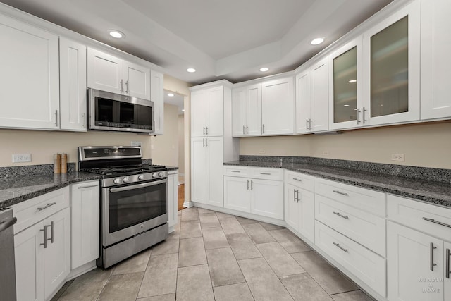 kitchen with a raised ceiling, white cabinetry, dark stone counters, light tile patterned floors, and stainless steel appliances