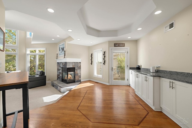 unfurnished dining area featuring a multi sided fireplace, plenty of natural light, a raised ceiling, and light hardwood / wood-style flooring