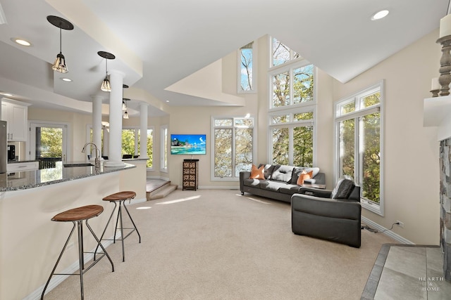 living room with sink, light colored carpet, decorative columns, and a high ceiling