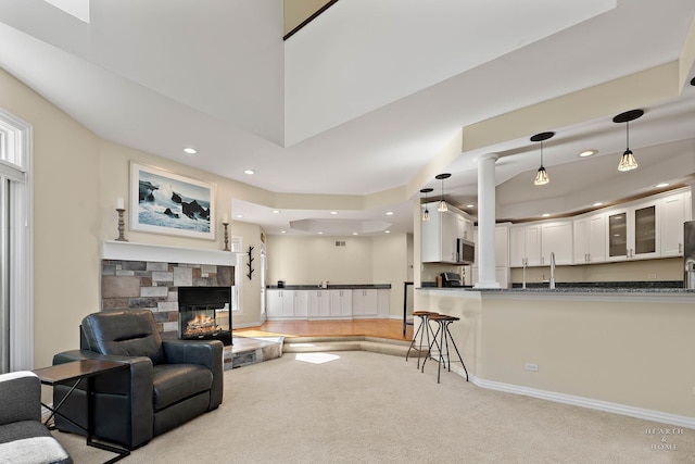 living room featuring a stone fireplace, light colored carpet, and decorative columns