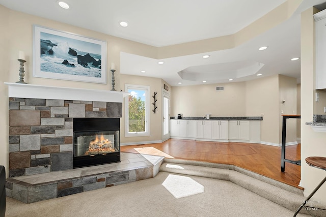 living room featuring light wood-type flooring, a raised ceiling, and a multi sided fireplace