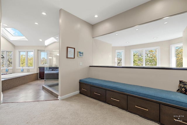 hall featuring light carpet, plenty of natural light, and vaulted ceiling with skylight