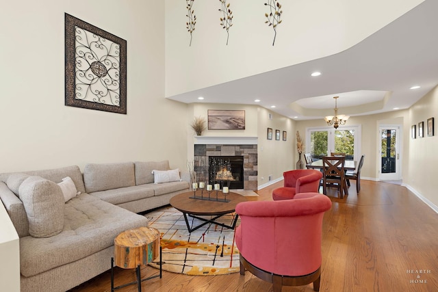 living room with a tray ceiling, a stone fireplace, hardwood / wood-style floors, and a notable chandelier