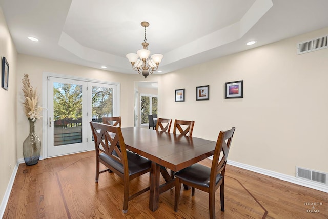 dining space with hardwood / wood-style flooring, a tray ceiling, and a notable chandelier