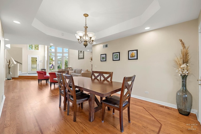 dining space with a notable chandelier, a raised ceiling, and light wood-type flooring