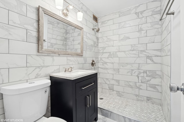 bathroom with vanity, a tile shower, tile walls, and toilet