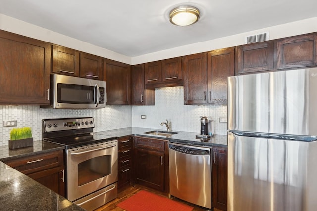 kitchen featuring appliances with stainless steel finishes, sink, backsplash, dark stone counters, and dark brown cabinets