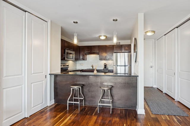 kitchen with dark brown cabinetry, dark hardwood / wood-style floors, pendant lighting, stainless steel appliances, and decorative backsplash