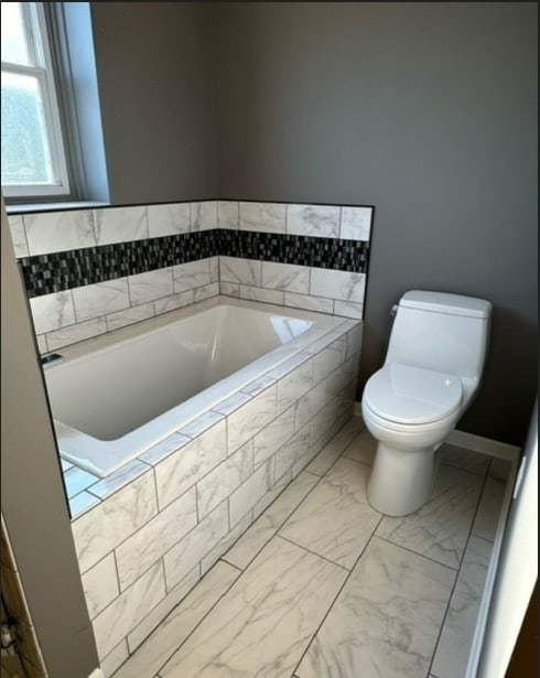 bathroom featuring tiled bath and toilet