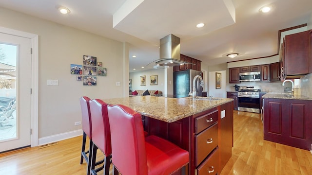 kitchen with sink, a breakfast bar area, light hardwood / wood-style floors, stainless steel appliances, and a center island with sink