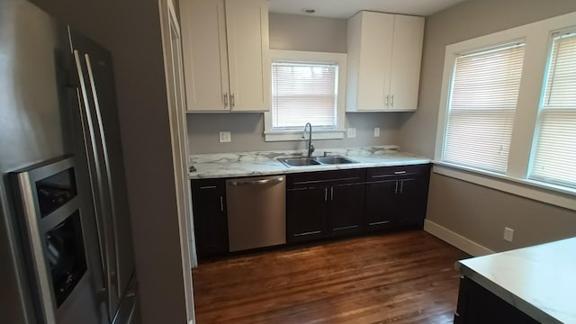 kitchen with sink, appliances with stainless steel finishes, light stone counters, white cabinets, and dark hardwood / wood-style flooring