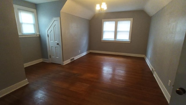 additional living space featuring dark wood-type flooring, an inviting chandelier, and vaulted ceiling