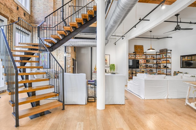 staircase with a high ceiling, brick wall, hardwood / wood-style floors, and ceiling fan