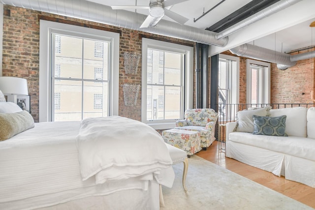 bedroom featuring hardwood / wood-style flooring, ceiling fan, and brick wall