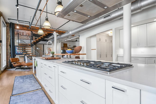 kitchen featuring light hardwood / wood-style flooring, rail lighting, hanging light fixtures, stainless steel gas cooktop, and white cabinets