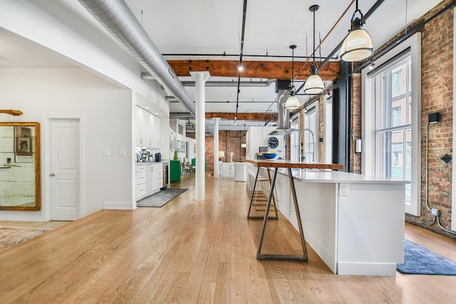 kitchen featuring brick wall, a breakfast bar, pendant lighting, white cabinets, and light hardwood / wood-style flooring