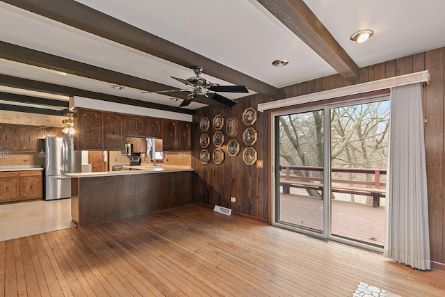 kitchen with stainless steel fridge, dark brown cabinetry, light wood-type flooring, kitchen peninsula, and wood walls