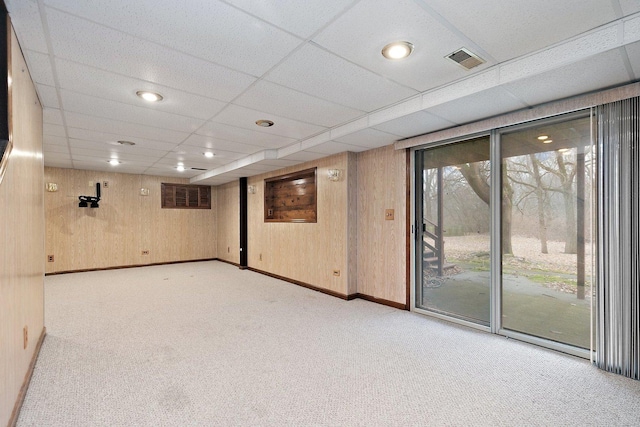 basement with light colored carpet, wooden walls, and a paneled ceiling