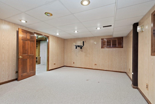 basement with light colored carpet, a drop ceiling, and wooden walls