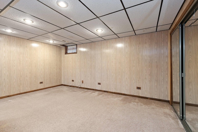 basement with light carpet, a drop ceiling, and wood walls