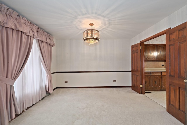 carpeted empty room with an inviting chandelier