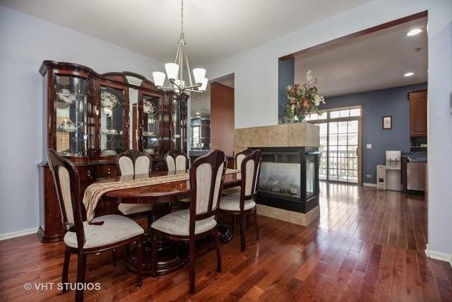 dining space featuring a tiled fireplace, dark wood-type flooring, and a chandelier